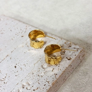Makroaufnahme goldbeschichteter unregelmäßiger C-Ohrringe mit Lavatextur auf Travertin