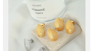 Detail of teardrop embossed metal earrings in gold and silver on marble base