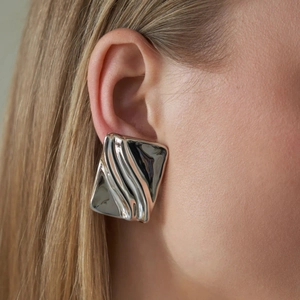 Close-up of a silver irregular square earring with a modern 3D wave texture on a model