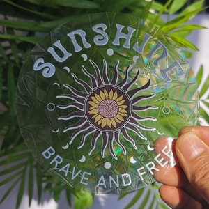 Macro view of holographic suncatcher sticker featuring a sunflower and sunshine engraving