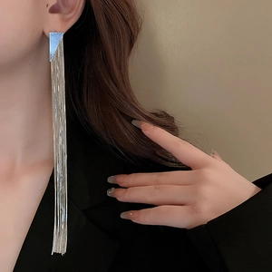 Model wearing geometric silver tassel earrings with long metallic chains and triangle top