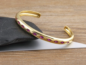 Detail of 18k gold plated cuff bracelet with marquise pink-purple zircons on wood