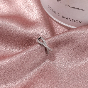 Minimalist silver crisscross ear cuff with micro-pave cubic zirconia on satin backdrop