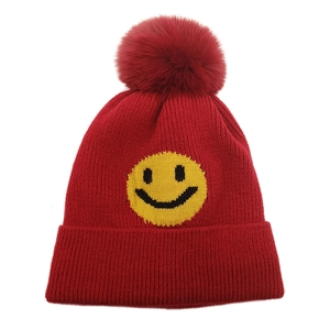 Detail einer roten Strickmütze mit gelbem Smiley und großem Kunstfell-Bommel für den Winter