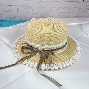 Detail of woven straw hat featuring white lace trim and dark brown checkered ribbon bow