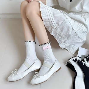 Detail of white ribbed JK socks with black wavy edges and a pink bow on the side