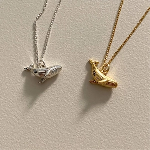 Close-up of minimalist silver and gold whale tail pendant necklaces with fine texture