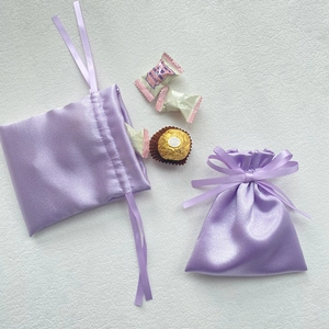 Close-up of two purple satin drawstring gift bags with smooth ribbon bows on a white surface