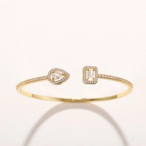Macro shot of gold adjustable open bangle featuring teardrop and rectangular cubic zirconia