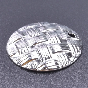 Macro view of a silver stainless steel round pendant featuring a detailed woven texture
