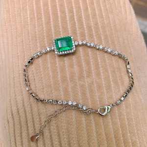 Close-up of silver chain bracelet with square green zircon and lobster clasp on corduroy