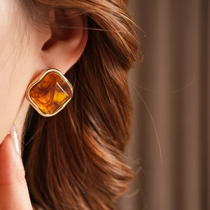 Close-up of amber resin diamond earring with golden metal frame on model ear