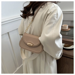 Chic light khaki leather saddle bag with gold chain strap shown on a woman in white coat
