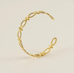 Detail shot of golden C-shaped bangle featuring cross and beaded oval openwork design
