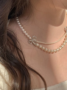 Détail d'un collier de perles à double rangée avec un pendentif nœud serti de strass