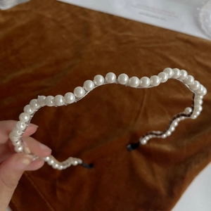 Close-up of white pearls on a transparent wavy headband with black fabric ends
