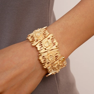 Detailed close-up of wide golden metal bracelet with embossed floral hollow pattern