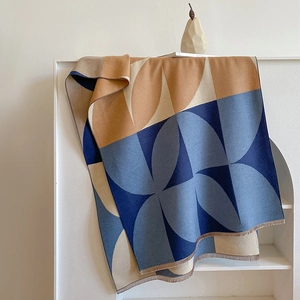 Detailed view of color-block knit scarf with decorative fringe on a white shelf