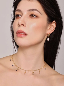 Detail of elegant gold necklace with colorful gemstones and white pearl earring on model