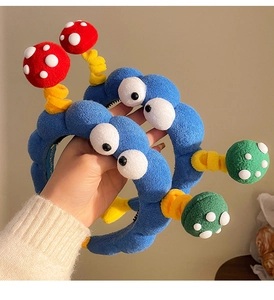Dettaglio di cerchietti in peluche blu con occhi a cartone e antenne a fungo colorate