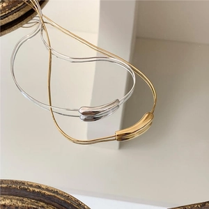 Close-up of gold and silver snake chain necklaces with curved pendants on a mirror surface