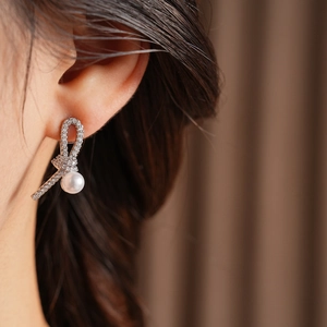 Gros plan de boucles d'oreilles nœud en argent avec zircons et une perle blanche