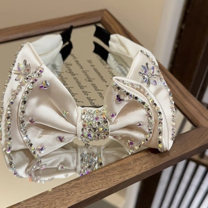 Close-up of luxury satin bow headband with sparkling rhinestones on a mirror surface