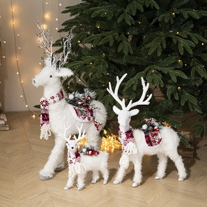 Three white Christmas reindeer figurines with red scarves near a festive tree