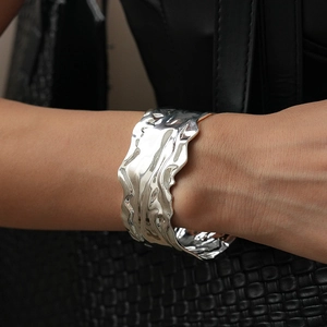 Macro detail of silver open cuff bracelet with irregular water ripple texture on wrist