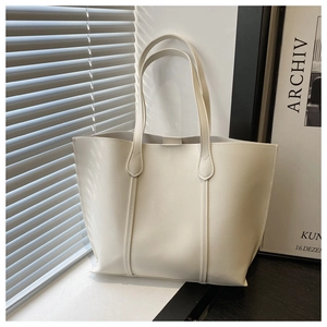 Detailed view of a cream-colored minimalist tote bag placed by a window in a bright room