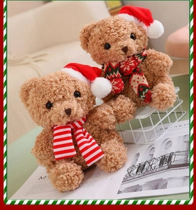 Close-up of two plush Christmas teddy bears with red hats and festive scarves on a cozy sofa