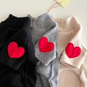 Close-up of knit pet sweaters with red heart patches in black, gray, and beige colors