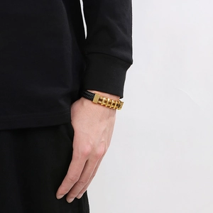 Dettaglio del bracciale da uomo in pelle nera intrecciata con chiusura dorata al polso