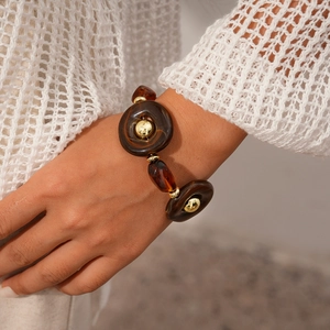 Detail of brown resin and gold metal sphere beaded bracelet on model's wrist