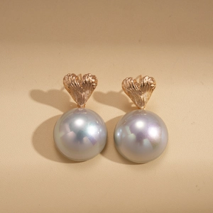 Close-up of heart-shaped gold studs with large iridescent pearls on a beige leather surface
