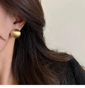 Detail of matte gold hemispherical stud earring with brushed metal texture on ear