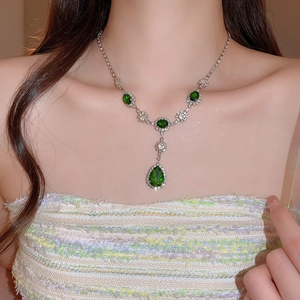 Dettaglio di una collana con pendente a goccia verde e cristalli indossata da una modella