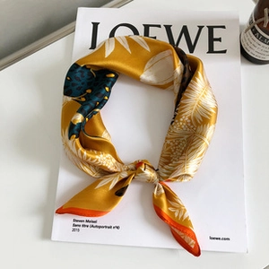 Close-up of luxury yellow silk scarf with botanical leaves placed on a fashion magazine