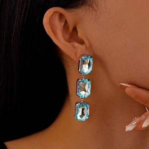 Macro shot of silver drop earrings with three tiered rectangular blue crystals on model