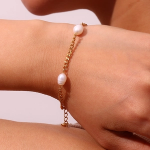 Detail of a gold Cuban chain bracelet featuring two white pearls on a model's wrist