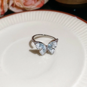 Close-up of light blue zircon butterfly ring with silver plating on white ceramic plate