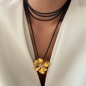 Detail of 18k gold floral pendant with crystals on black leather cord on a model