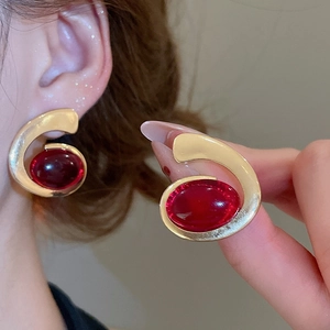 Detailed close-up of a gold spiral earrings set with red oval resin gemstones for women