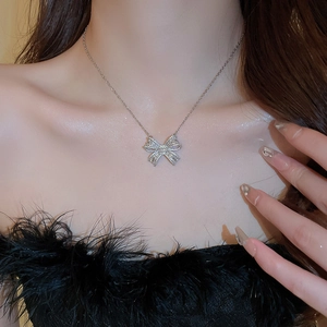 Detail of zircon bow pendant on silver chain worn on neck with black feather accents