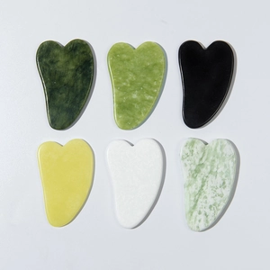 Flat lay of heart-shaped jade facial gua sha tools in diverse natural mineral colors