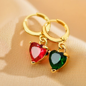 Macro shot of gold hoop earrings with red and green zircon heart pendants on soft fabric
