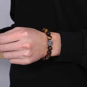 Detail of tiger eye beaded bracelet featuring a steel skull and cross charm on wrist