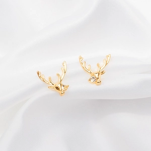 Close-up of golden reindeer stud earrings with sparkling zircon on silk background