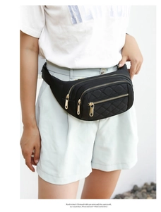 Close-up of quilted black fanny pack with gold zippers and three layered compartments