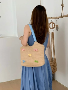 Detail of hand-woven straw shoulder bag with colorful yarn bow accents and blue strap